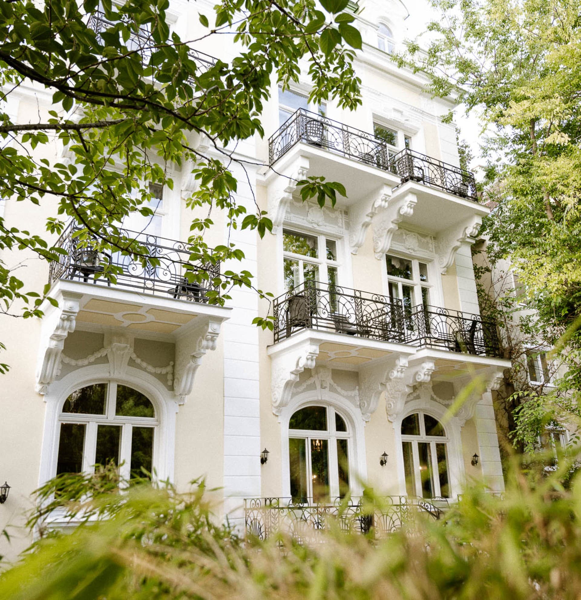 Gezeigt wird die Außenansicht des Hideauts Hotels Villa R, das sich durch seine wunderschön zum Garten hin gelegenen Balkone auszeichnet.