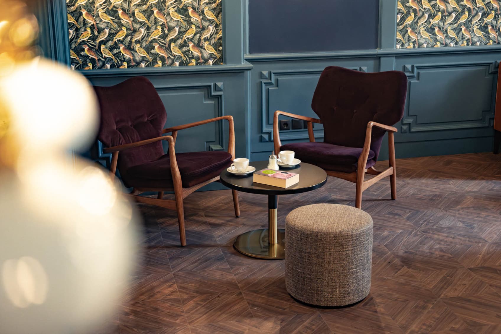 The lounge invites guests to stay for a coffee and have ba slice of cake in the afternoon or meet up with friends in the evening and chill. The colours are warm and dark blue, bourdeaux and the wallpaper are birds.