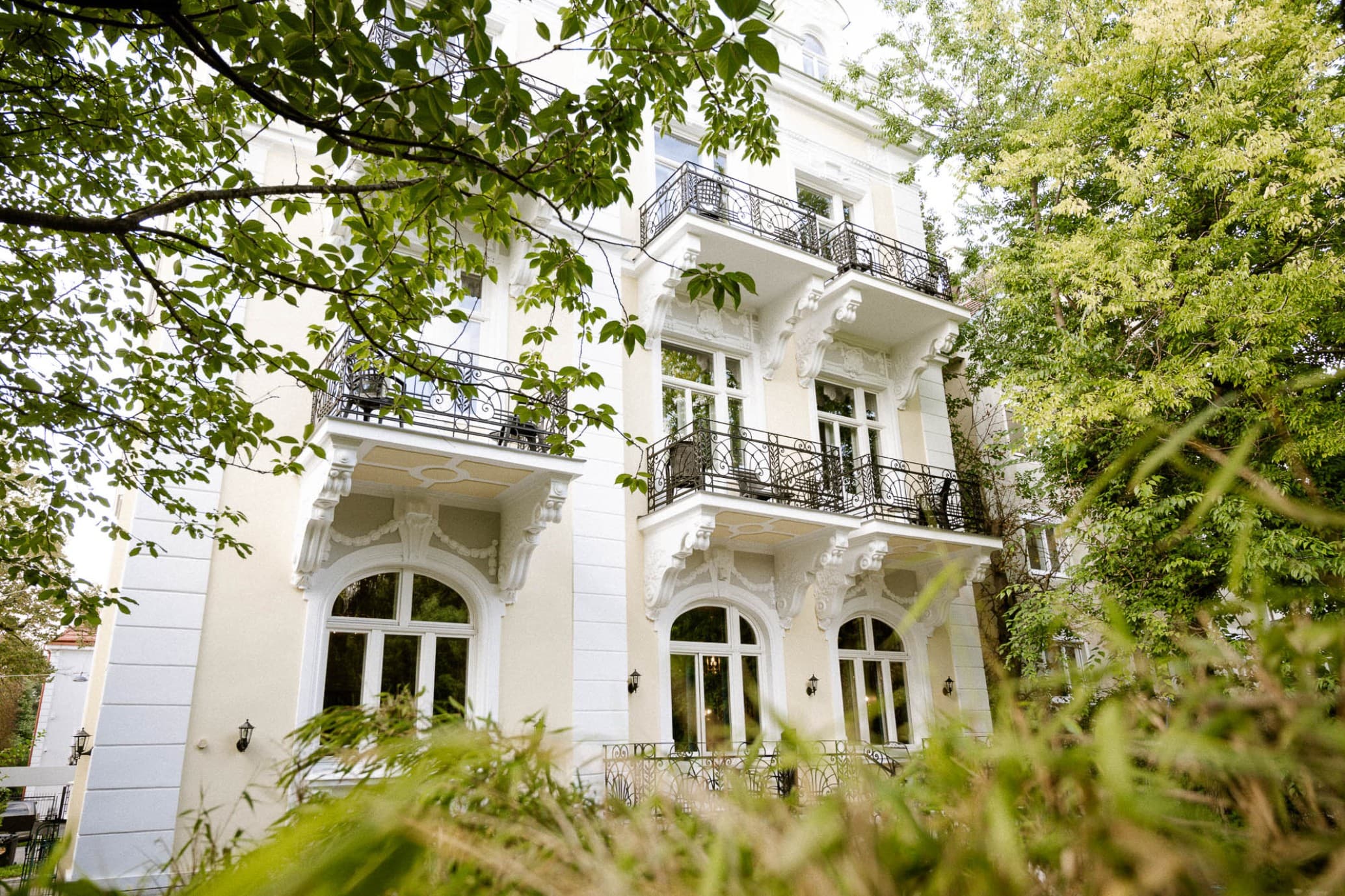 Zu sehen ist die Außenseite der Villa R mit Blick auf die Rückseite der Villa und die Balkone. Durch den Garten hindurch fotografieren.