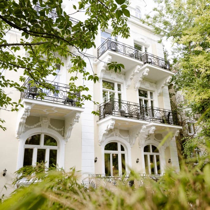 Zu sehen ist die Außenseite der Villa R mit Blick auf die Rückseite der Villa und die Balkone. Durch den Garten hindurch fotografieren.