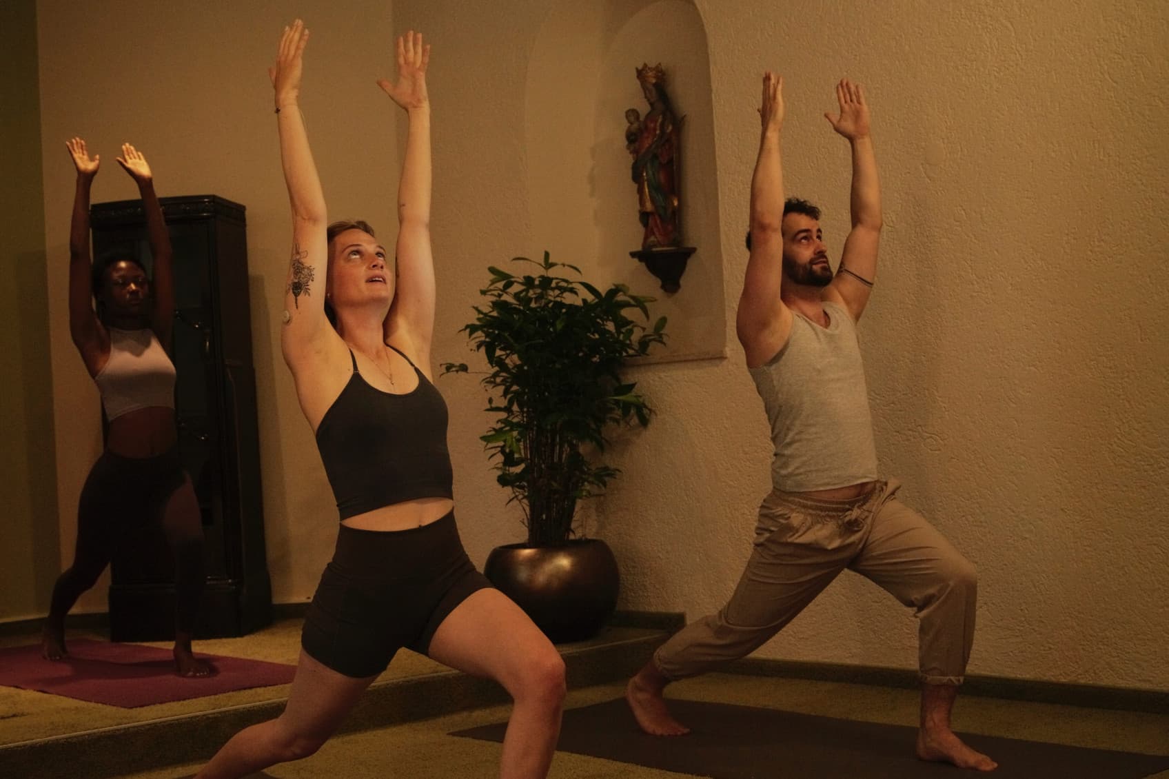 Seen are two people, who are part of a YOGA session. They are doing a pose, where they put up their arms and breathe out. Its situated in a YOGA room at the hideauts hotels Der Rosengarten.