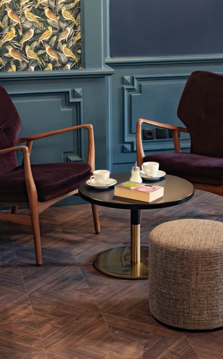 Die Lounge lädt Gäste dazu ein, nachmittags auf einen Kaffee und ein Stück Kuchen vorbeizukommen oder sich abends mit Freunden zu treffen und zu entspannen. Die Farben sind warm und dunkelblau, bordeauxrot, und die Tapete ist mit Vögeln verziert.