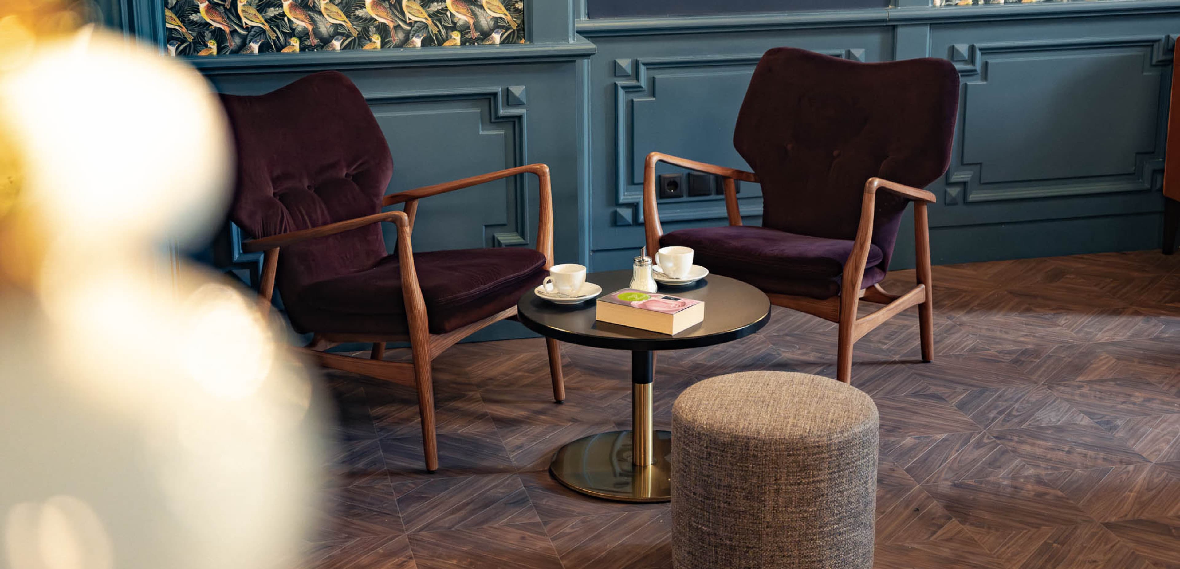 Die Lounge lädt Gäste dazu ein, nachmittags auf einen Kaffee und ein Stück Kuchen vorbeizukommen oder sich abends mit Freunden zu treffen und zu entspannen. Die Farben sind warm und dunkelblau, bordeauxrot, und die Tapete ist mit Vögeln verziert.