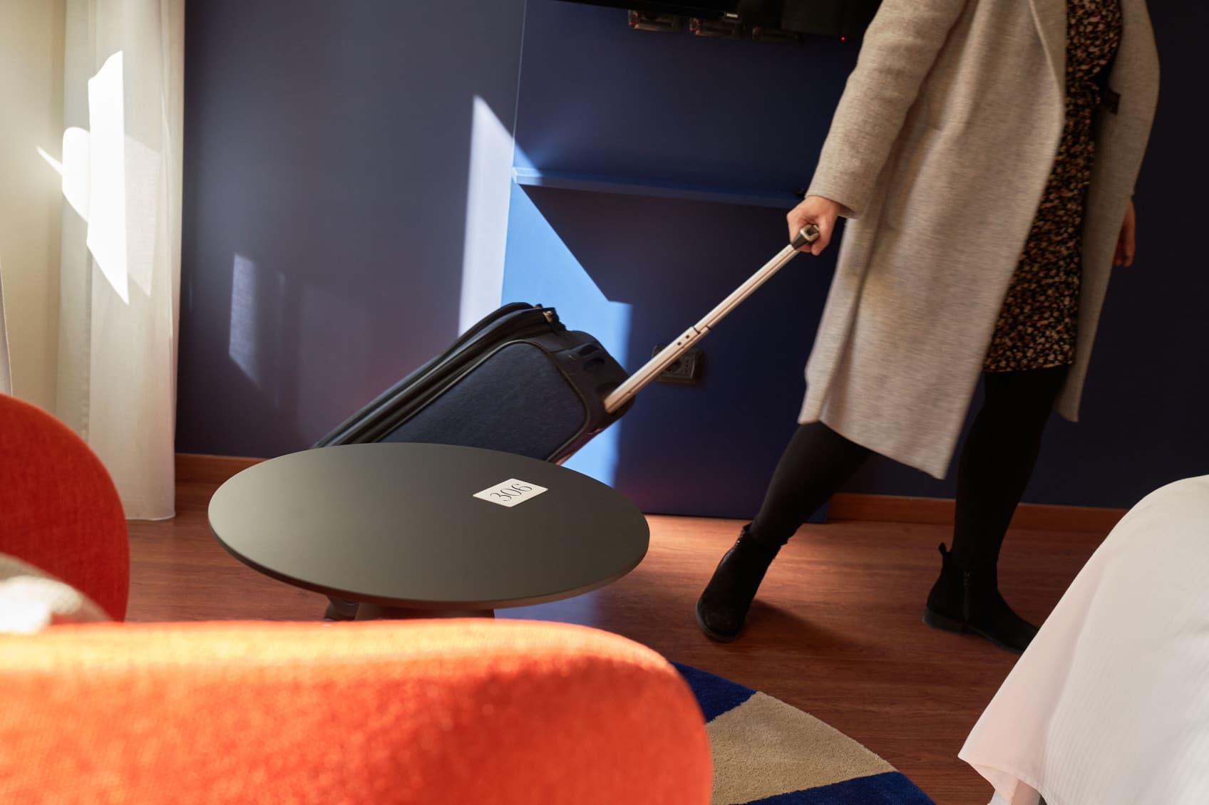 woman who is pulling a suitcase into teh room at Villa R. She is wearing a beige coat.