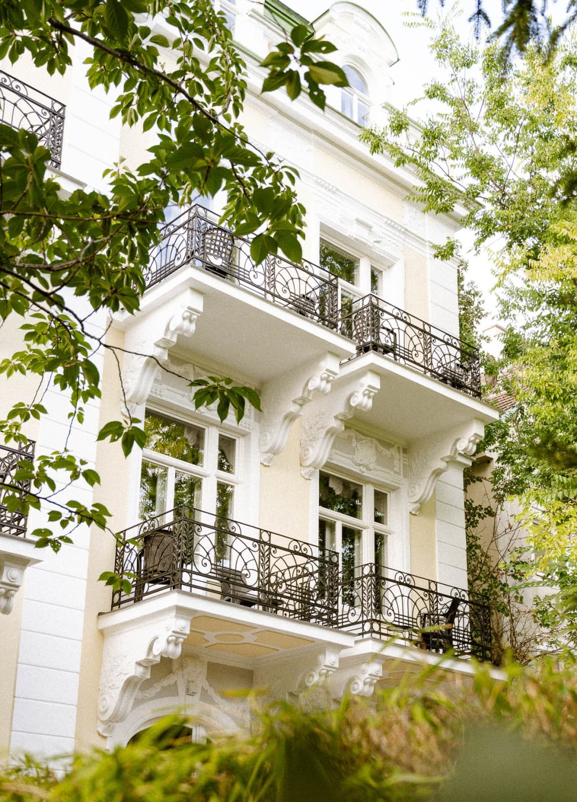 Seen is the exterior of the historic Villa from the backyard. Nestled between trees and bushes, the newly rennovated facade shows the beauty of the Villa.