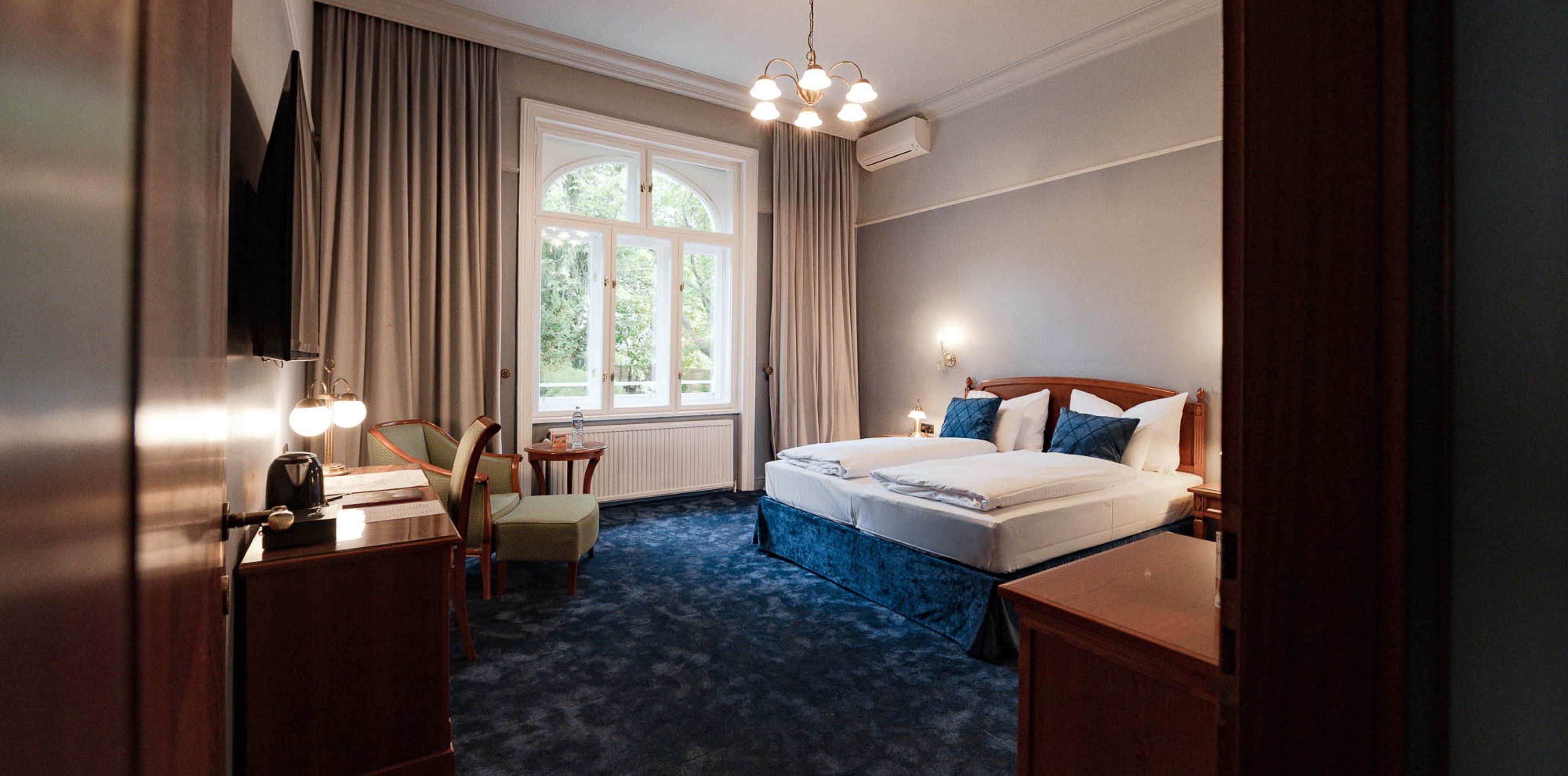 Das Bild zeigt eine Gesamtansicht der Kategorie „Chic Garden View“, in der das Doppelbett auf der rechten Seite und die Tür zum Balkon geradeaus zu sehen sind.