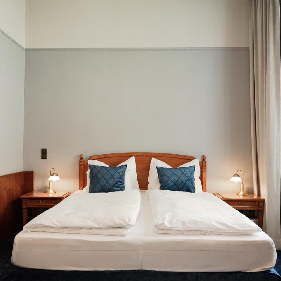 Das Bild zeigt die Seite des Zimmers mit dem Doppelbett. Die Kategorie „Comfy“ ist für zwei Personen ausgelegt und verfügt zusätzlich über eine kleine Couch. Auf der linken Seite ist ein Gemälde einer Frau im Art-déco-Stil zu sehen.