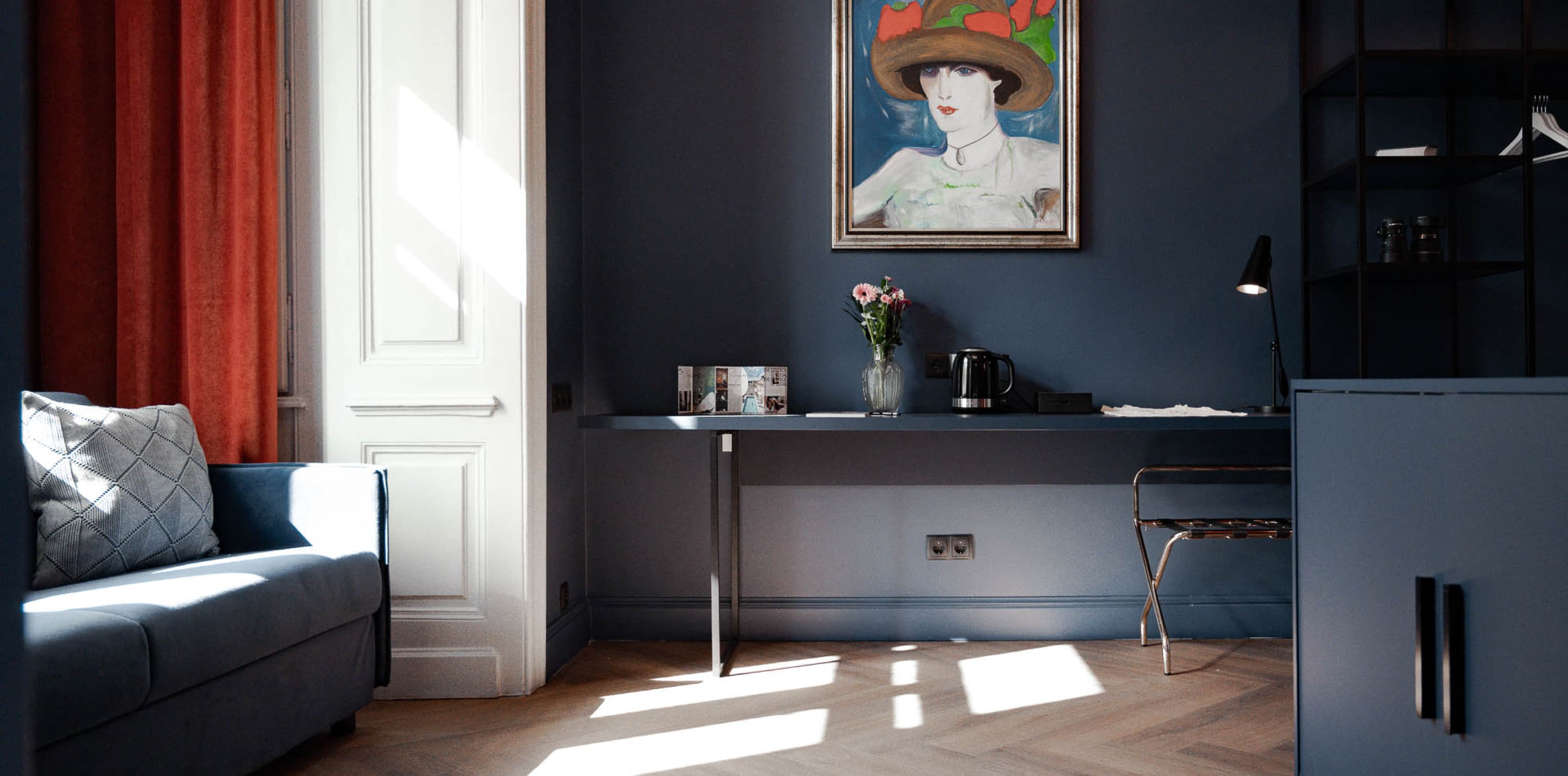 Pictured is the spacious living area of the Spacy category. It offers plenty of space for a couch on the left side, cupboards on the right and a desk to work at straight ahead. All is painted in a dark blue colour.