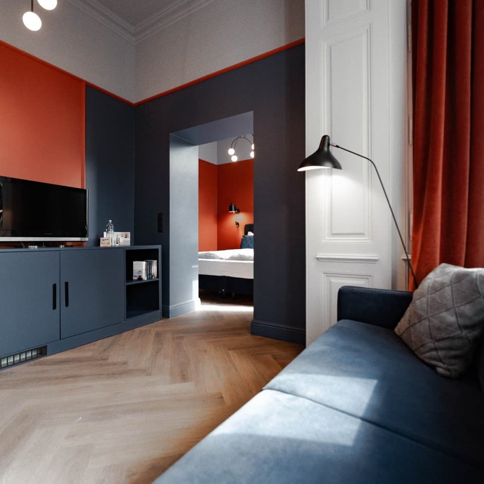 Zu sehen ist die Kategorie „Spacy“ und der Blick von der Couch in Richtung Schlafzimmer. Die größte Kategorie bietet ein Schlafzimmer sowie ein separates Wohnzimmer. Auch hier sind die Farben Orange und Blau präsent.