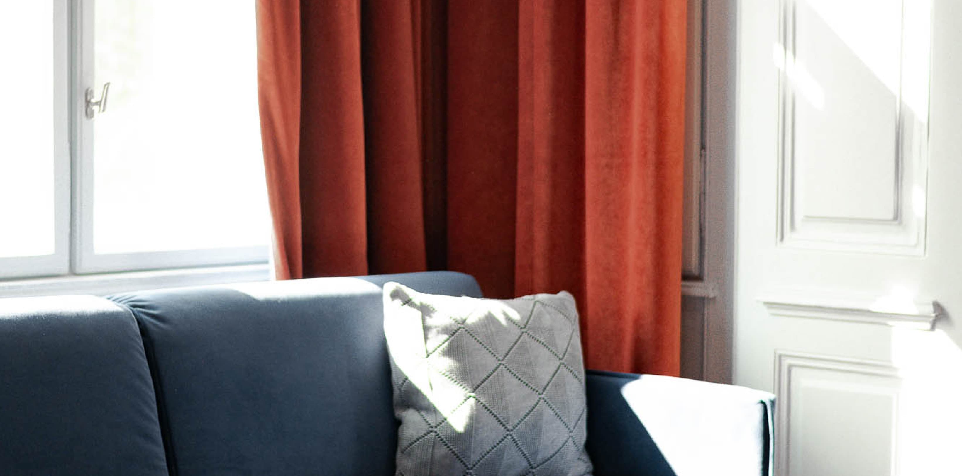The couch in the living area offers a perfect spot for the afternoon. Take break and rest on the dark blue couch in front of a dark orange curtain.
