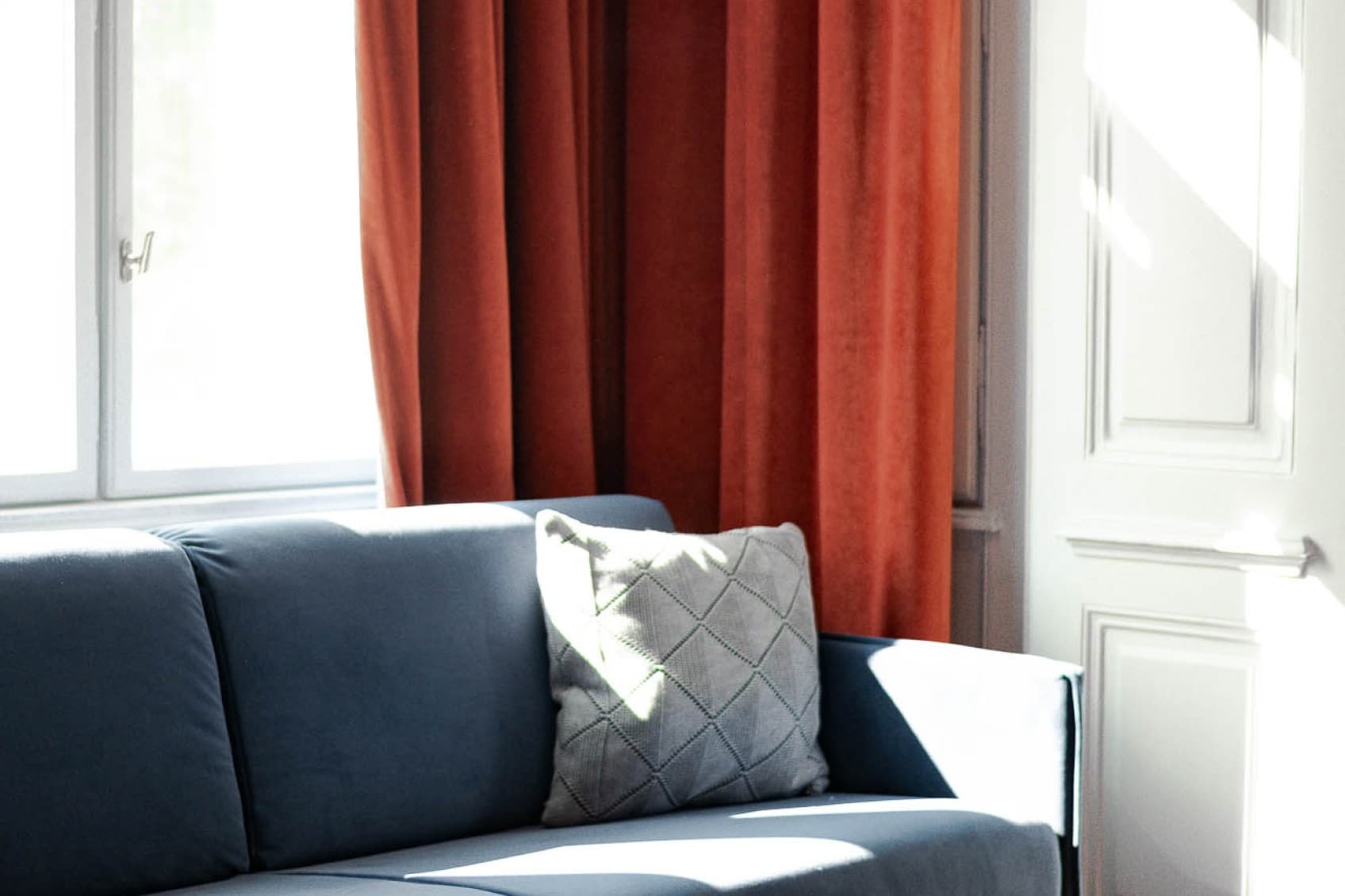 The couch in the living area offers a perfect spot for the afternoon. Take break and rest on the dark blue couch in front of a dark orange curtain.