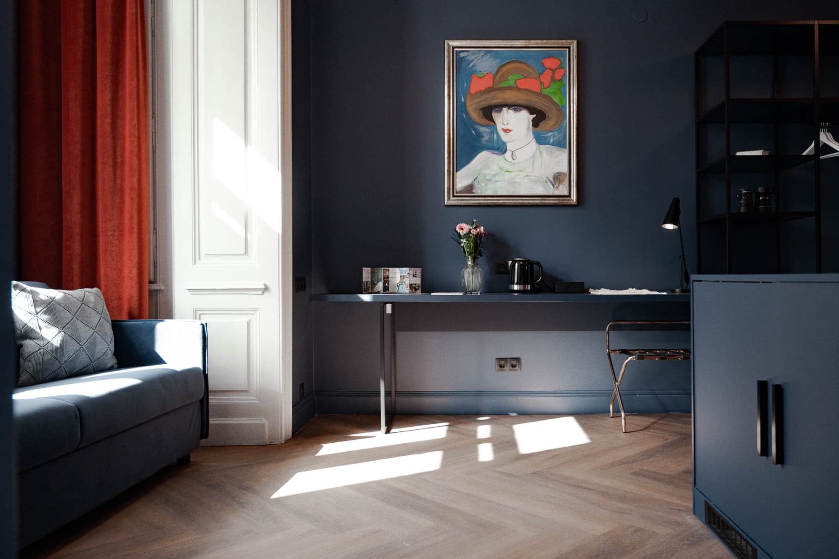 Pictured is the spacious living area of the Spacy category. It offers plenty of space for a couch on the left side, cupboards on the right and a desk to work at straight ahead. All is painted in a dark blue colour.