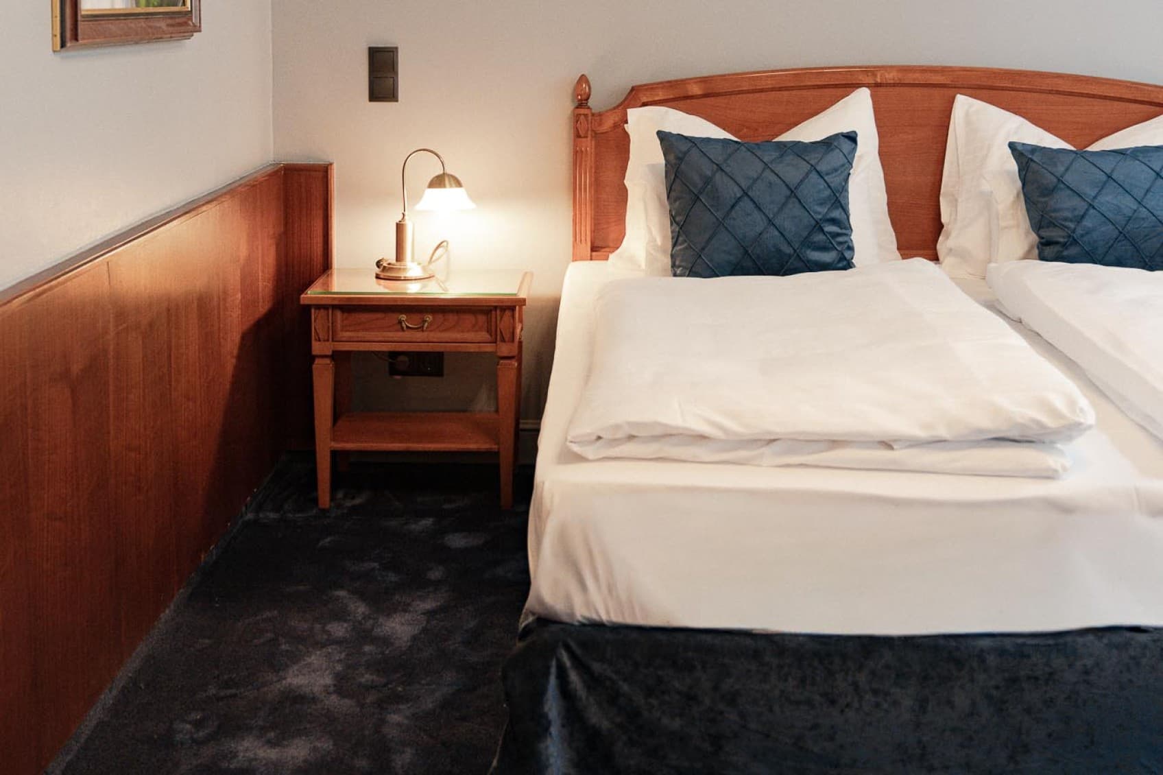 Seen is a possible picture of a Spacy Category, which shows the bed on the right side, a art piece hanging on the left side and a blue carpet.